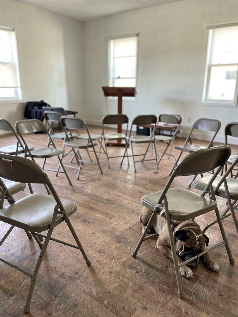 A folding table at the front of a rented meeting room with a gavel, a printed agenda, and a stack of show entry forms beside a thermos.
